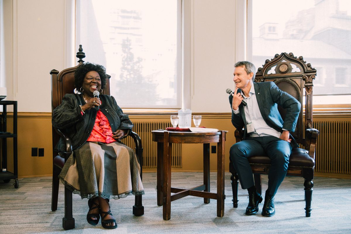 Dr. Jean Augustine sits in a chair, speaking with Chancellor Nick Saul during a Charter Day event.