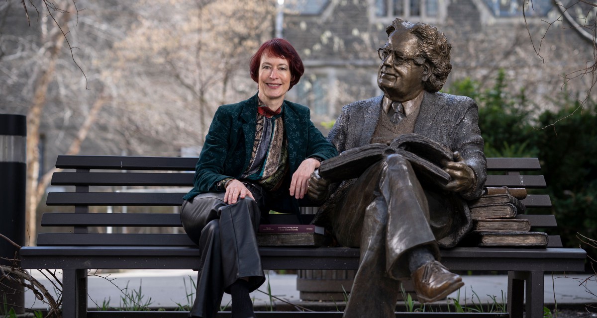  Principal Angela Esterhammer sits next to a bronze statue of Northrop Frye.