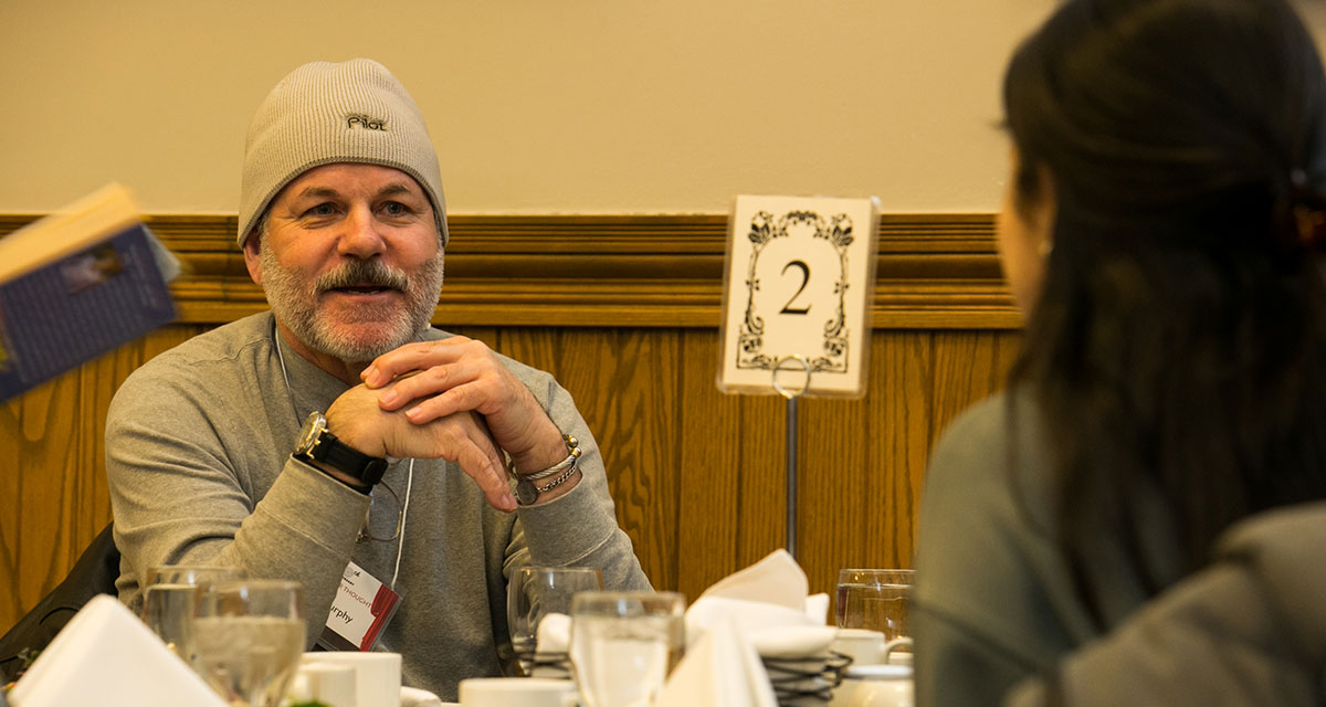 A man and a woman engage in a thoughtful exchange of ideas while seated at a table during a Humanities for Humanity event at Alumni Hall, Victoria University, University of Toronto.