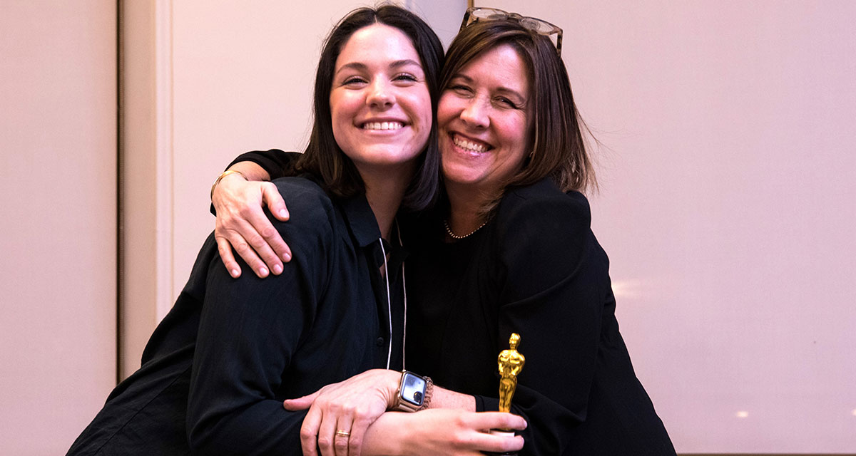 Dean Kelley Castle and student Naomi Trick share an embrace while holding a miniature Oscar statue during a Humanities for Humanity event at Victoria University, University of Toronto.